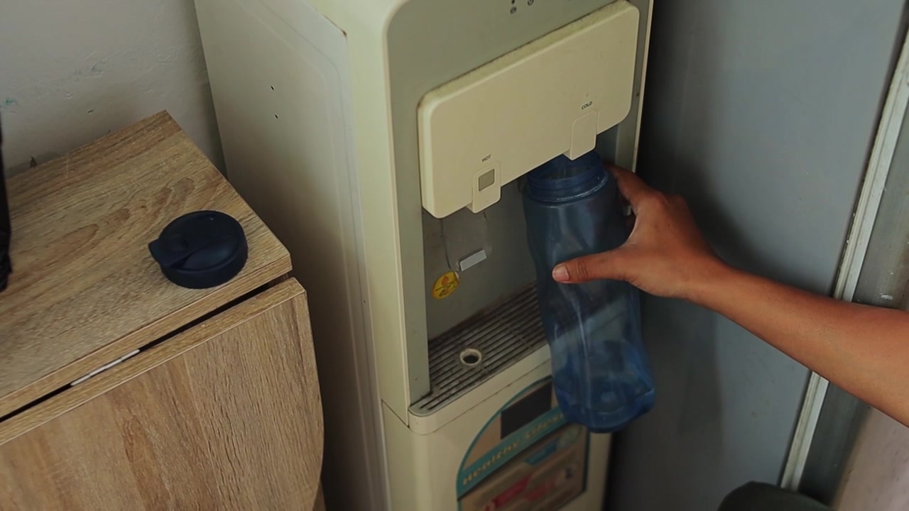 Personne remplissant une bouteille d'eau réutilisable bleue à un distributeur d'eau au bureau ou à la maison