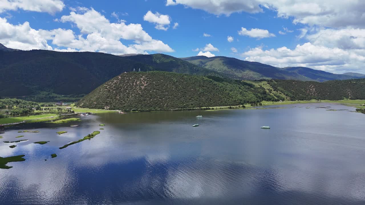 Filmagem aérea deslumbrante do Lago Napahai em Shangri-La, apresentando água azul clara refletindo nuvens brancas, cercado por montanhas e colinas verdes exuberantes.