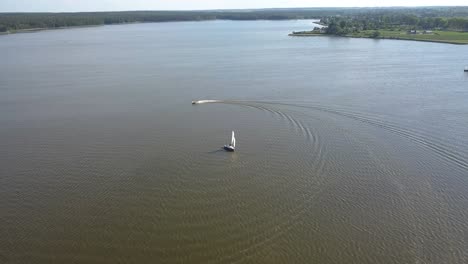 Toma-Aérea-Inclinada-Hacia-Abajo-De-Un-Velero-Y-Una-Moto-De-Agua-Navegando-En-Un-Lago-De-Lublin,-Polonia