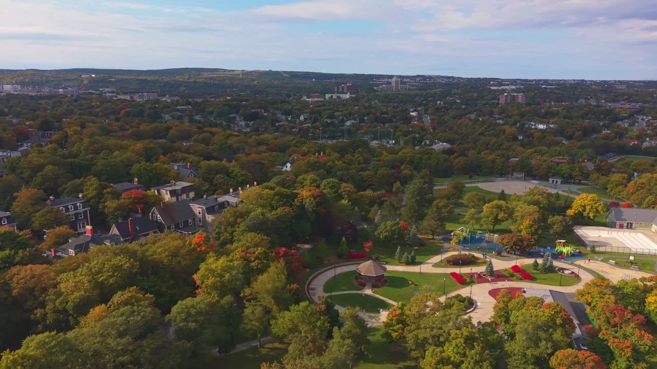 Urban aerial of St. John’s park with figure‑eight path, playground and autumn trees; Victorian homes and skyline frame the greenery