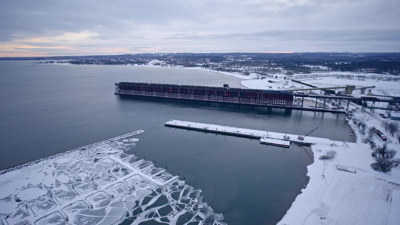 Ripresa con drone che sorvola il Lago Superiore parzialmente ghiacciato verso un molo di carico di minerale di ferro nel Michigan settentrionale