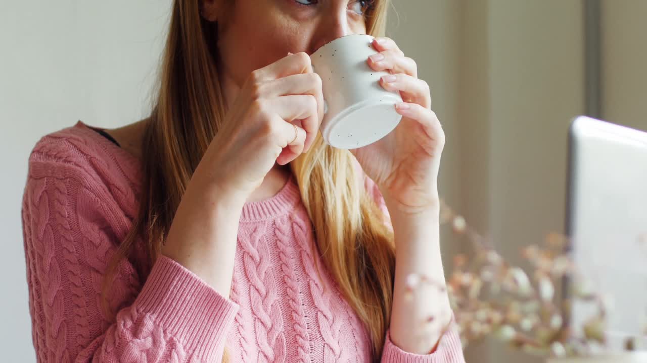 mujer pensativa tomando té mientras usa una computadora portátil 4k