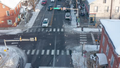 Amish-horse-and-buggy-pass-through-busy-town-intersection-in-Lancaster-County,-PA,-aerial-winter-scene-with-snow