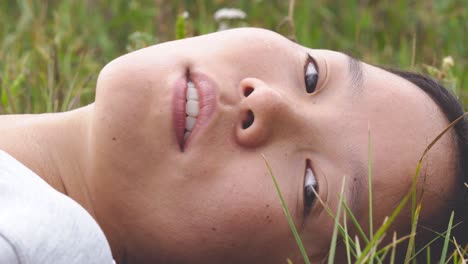 beautiful ethnic asian chinese mongolian woman lays in grass turning head with soft smile, perfect complexion