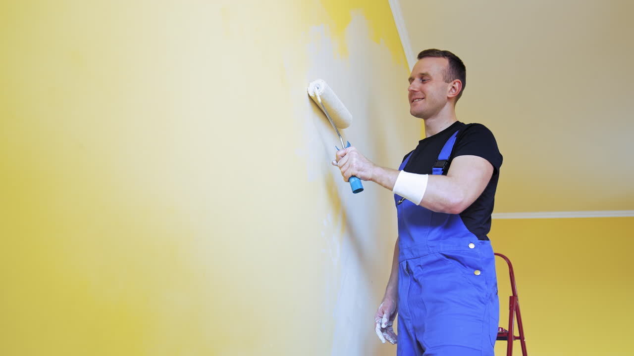 Man painting walls at home. Handsome man in work overalls paints the wall with a roller