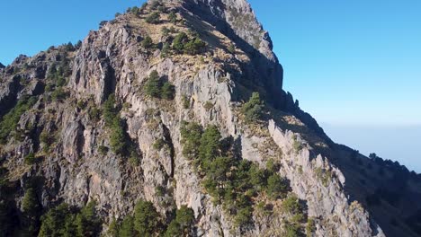 Toma-Aérea-Alejándose-De-Un-Pico-De-Montaña-Rocosa-Y-Un-Bosque-En-México-Durante-El-Día-En-Lugares-De-Senderismo-De-Verano-En-Estados-Unidos