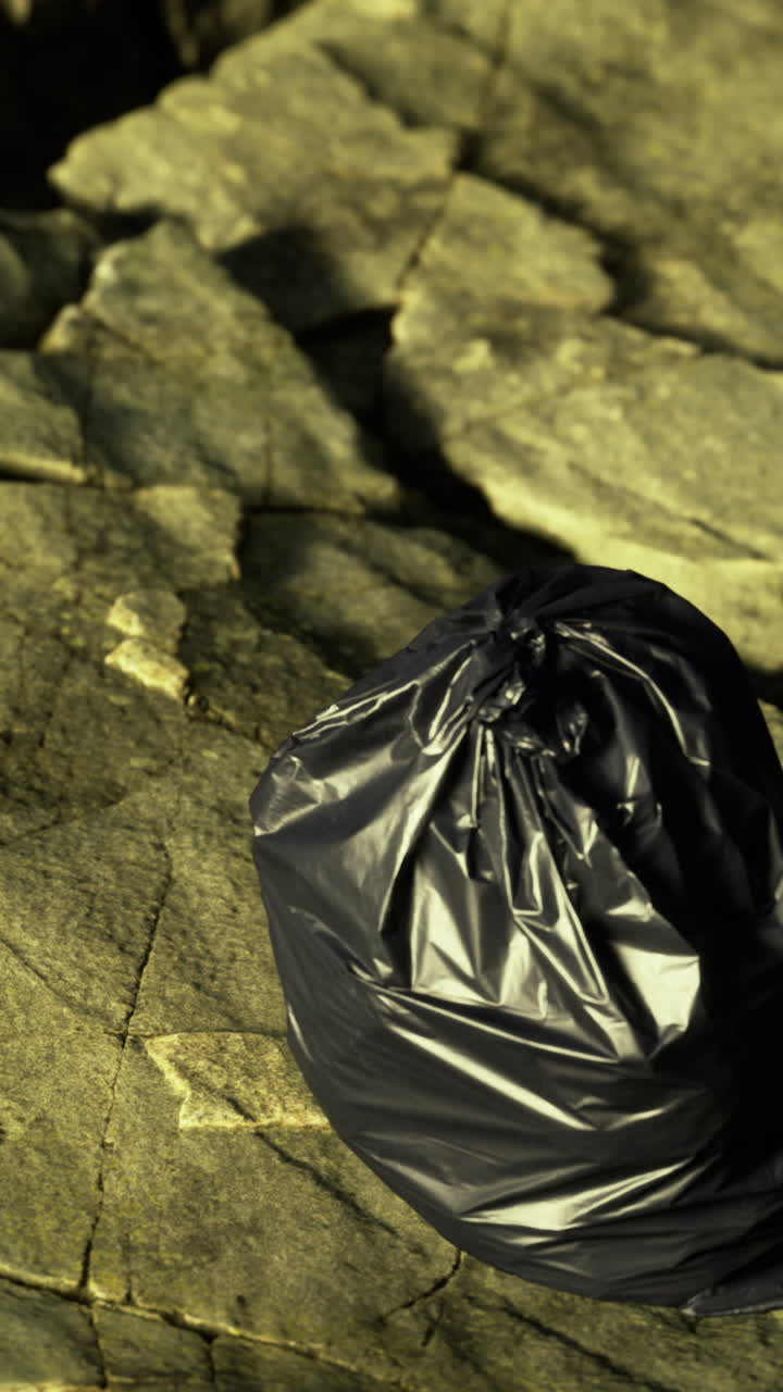 Borsa nera lasciata su una superficie rocciosa vicino all'acqua durante il giorno.