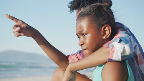 happy african american mother sitting with daughter on sunny beach