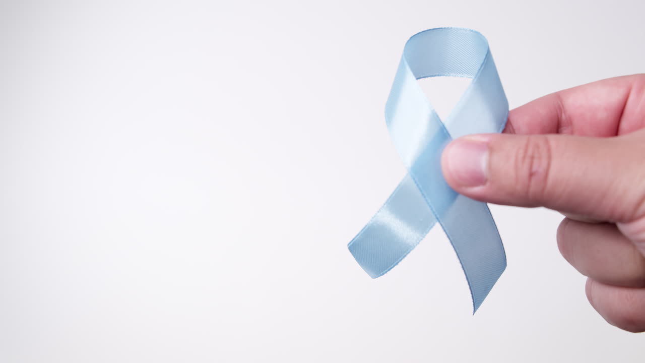 Dettaglio di mano maschile che posiziona un nastro di colore azzurro chiaro su sfondo bianco
