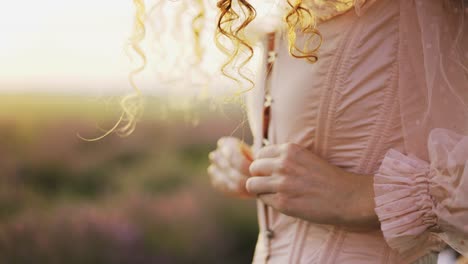 Curly-haired-girl-in-a-pink-dress-opens-buttons-on-corset-among-a-purple-field