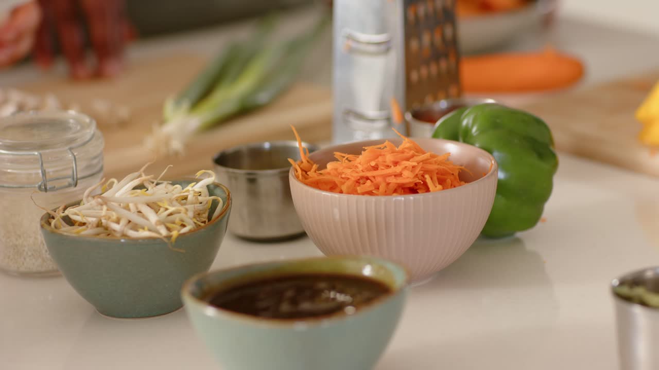 3 kitchen bowls holding center while camera shifting right, hand reaching, showing grater, peppers