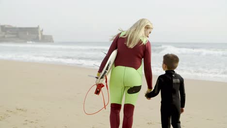 madre e hijo en trajes de neopreno caminando por la playa