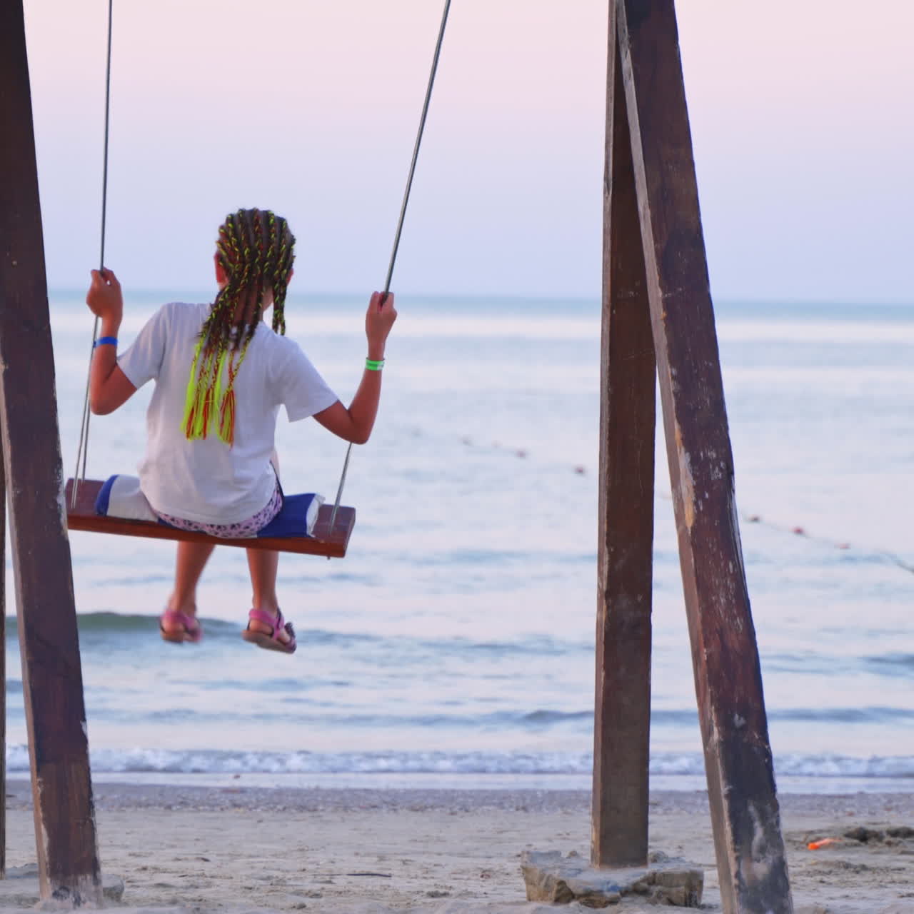 Girl enjoying a beautiful sea landscape on a swing. Young female resting alone near water. Back view of a girl swinging against the sea background in the evening.