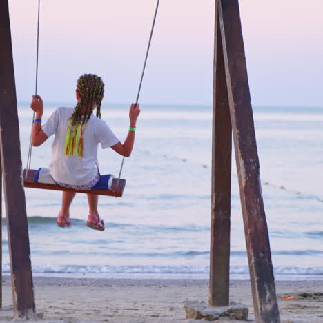 girl enjoying a beautiful sea landscape on a swing. young female resting alone near water. back view of a girl swinging against the sea background in the evening.