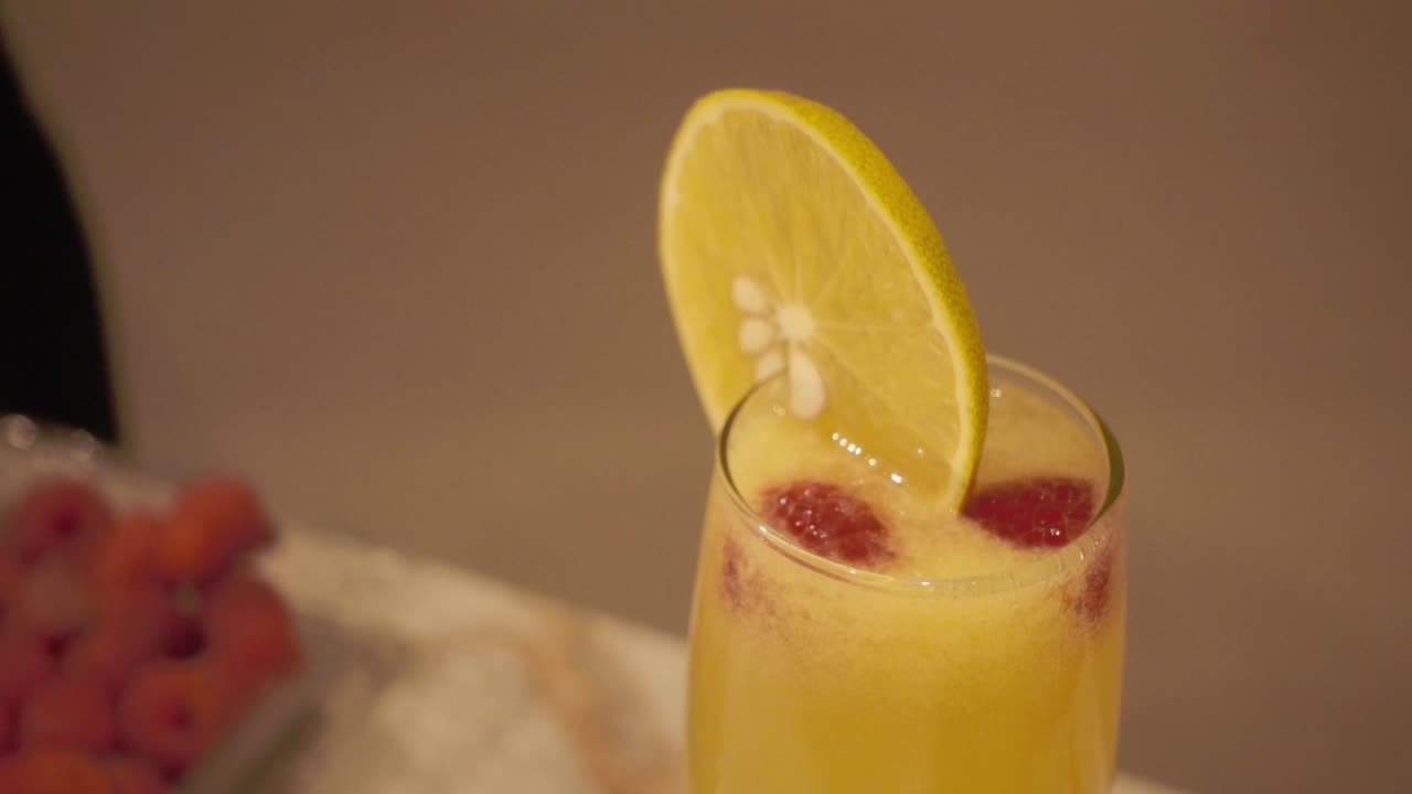 Primo piano di un cocktail agli agrumi dai colori vivaci, guarnito con una fetta d'arancia e frutti di bosco. L'illuminazione calda esalta i colori vibranti e l'aspetto rinfrescante della bevanda.
