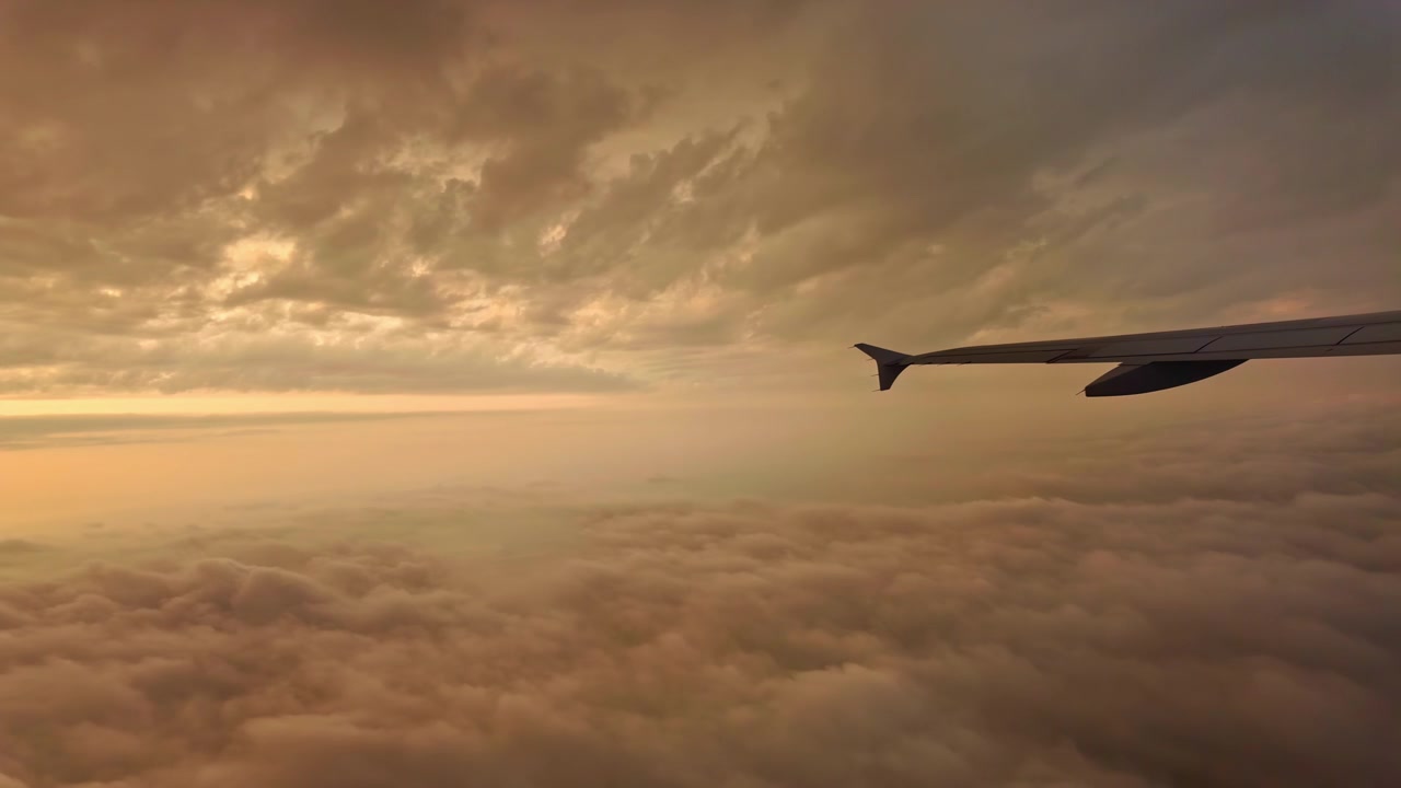 Flyet beveger seg blant lagskyer, utsikt fra flyvinduet. Vingen på et passasjerfly skjærer gjennom rosaaktige skyer ved solnedgang