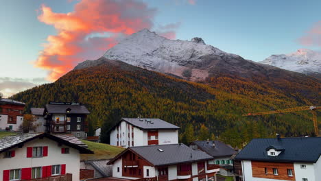 early morning vibrant colorful sunrise orange pink cloud above swiss alps snow dusting mountain peaks saas fee zermatt saastal alpine valley chalet ski resort town crane switzerland europe static shot