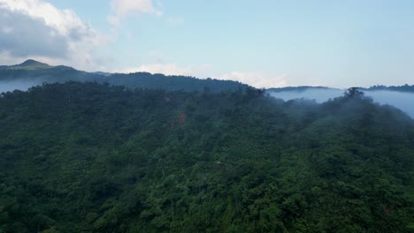 Mountain-background-with-misty-white-cloud-fog-hanging-below-ridgeline,-aerial-dolly