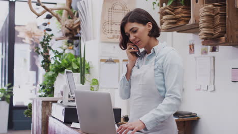 asistente de ventas femenina tomando una llamada telefónica detrás del mostrador de ventas de la tienda de flores