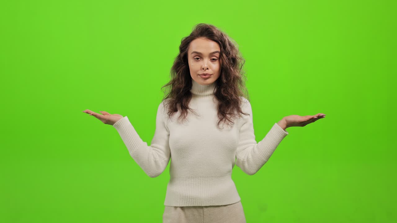 The woman is standing and looking at the camera. She is waving her hands and waving her head that she doesn't know. She is standing on a green background. Green screen. 4K.