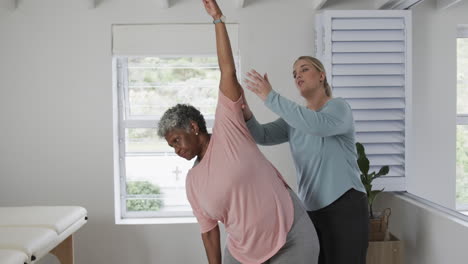 caucasian female physiotherapist with senior woman exercising, copy space, slow motion