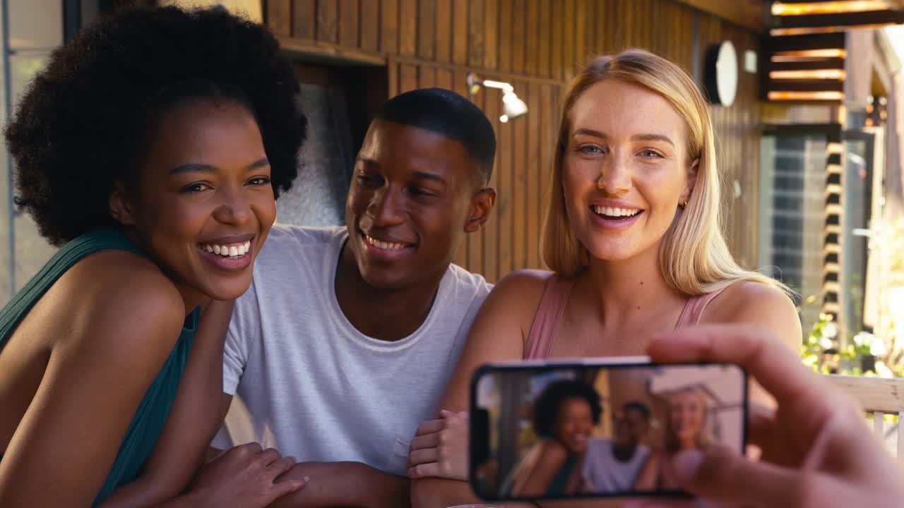 grupo de amigos multiculturales sonrientes al aire libre en casa posando juntos para una foto en el teléfono móvil