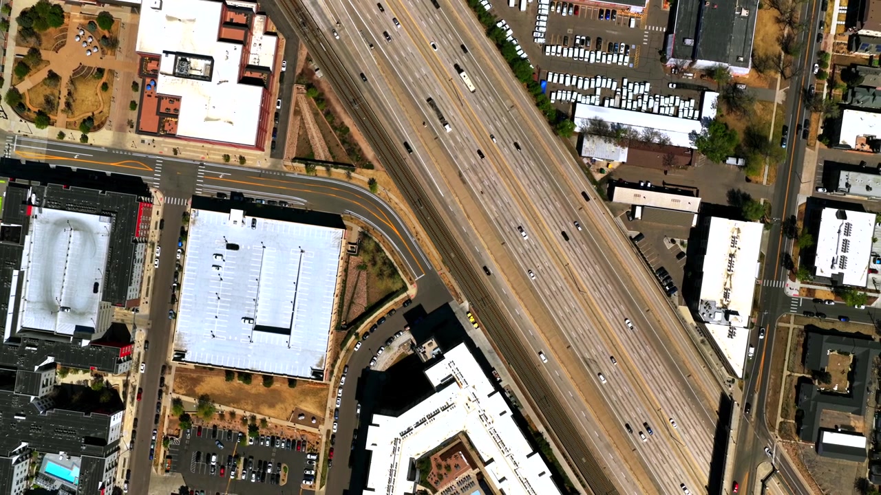 Traffico di auto sulla strada i25, autostrada a due corsie, nel centro di Denver, Colorado, in una soleggiata mattina di primavera. Vista aerea con drone a volo d'uccello del panorama urbano, dello scalo ferroviario Burnham Yard e degli edifici del Front Range, con movimento verso l'alto.