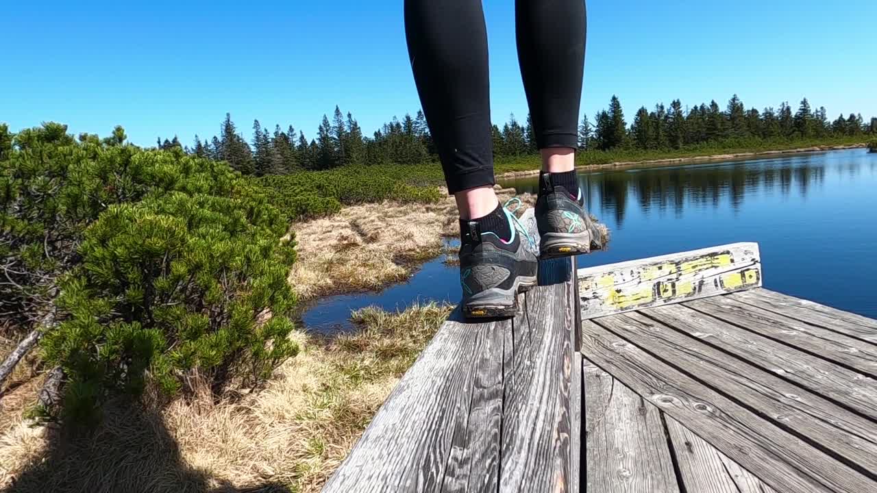 Lower part of woman's legs in low hiking shoes walking away  on a wooden fence by the lake slow motion