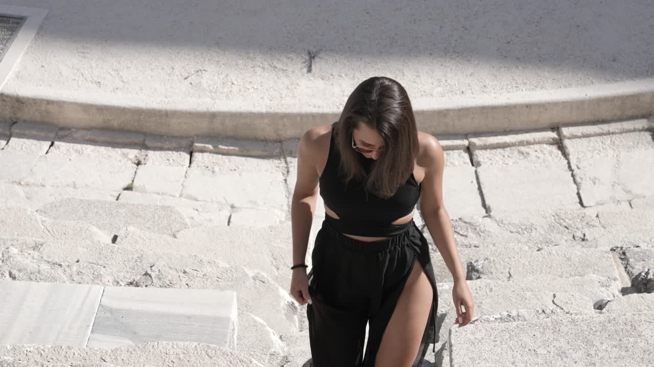 Young Woman in Black Dress Walking on Steps in Ancient Roman Theatre Auditorium, Close Up