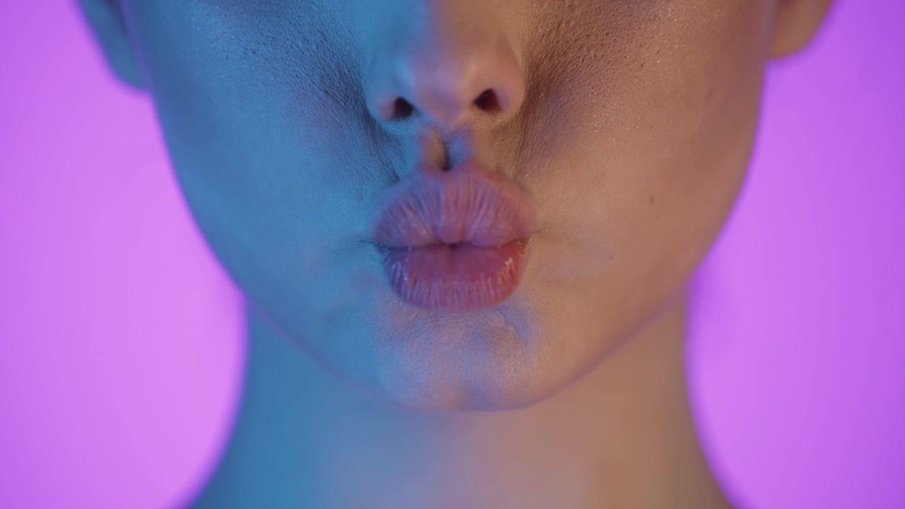 Primo piano della bocca e delle labbra di una donna che si baciano, scatto in studio con sfondo rosa.
