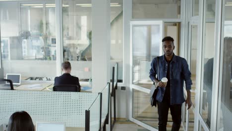 african american man walking with coffee into office