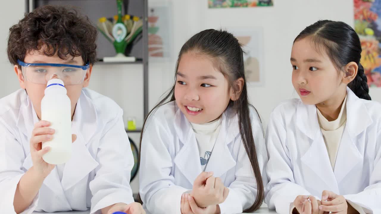 白衣とゴーグルを着用した若いアジア系の生徒3人が、牛乳を使った化学実験を行っています。