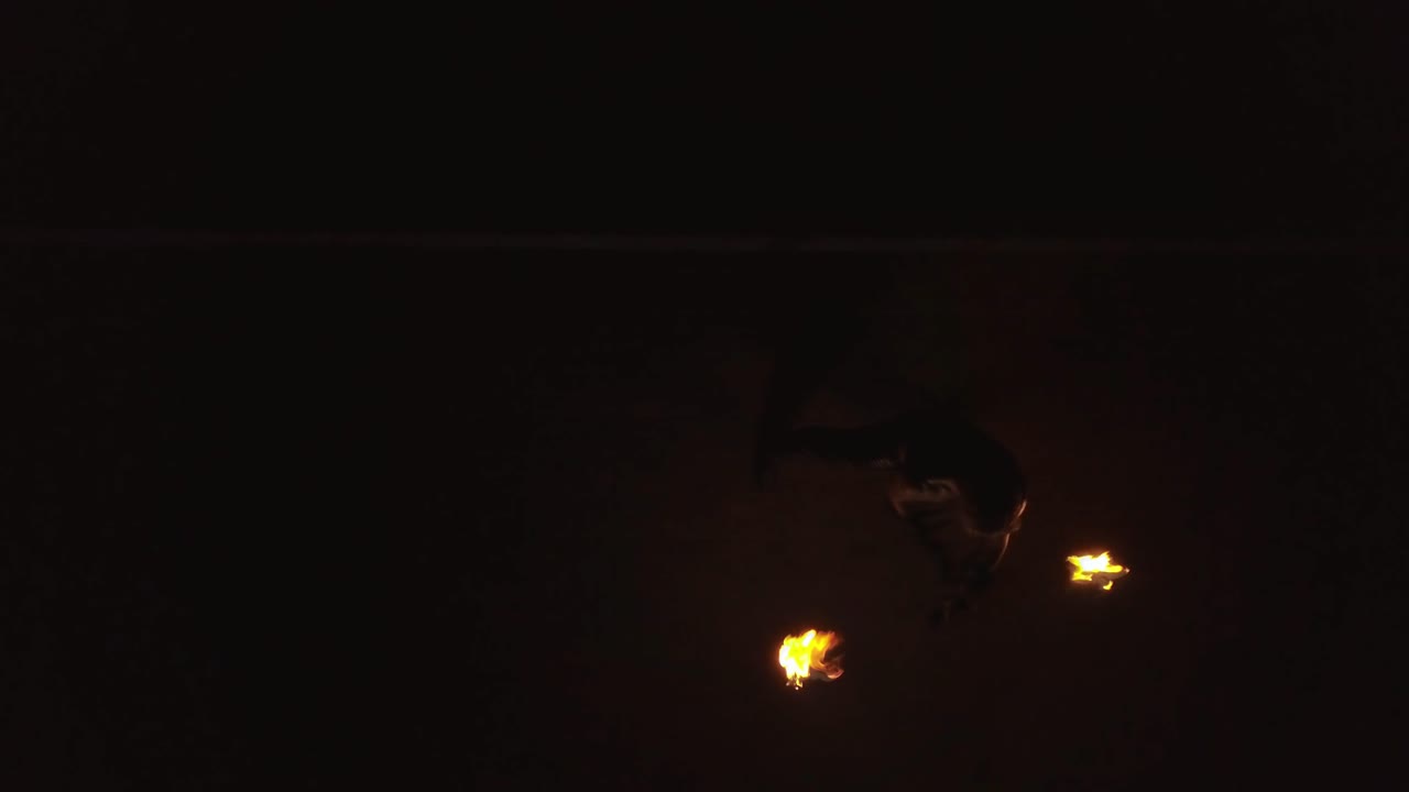 Young blond male does fire dance with two torches spins burning torches Aerial
