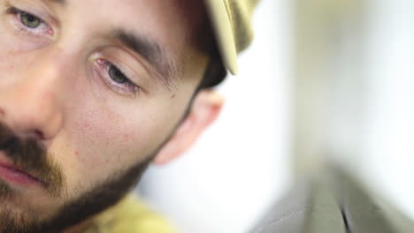 close up bearded caucasian male with blue eyes wearing hat reading news on smartphone with blurred background