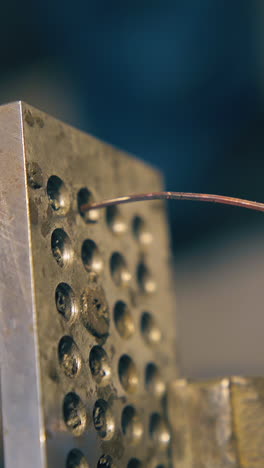 cu: skilled silversmith pulls metal wire through hole in tool with old pliers at workplace in light workshop close view
