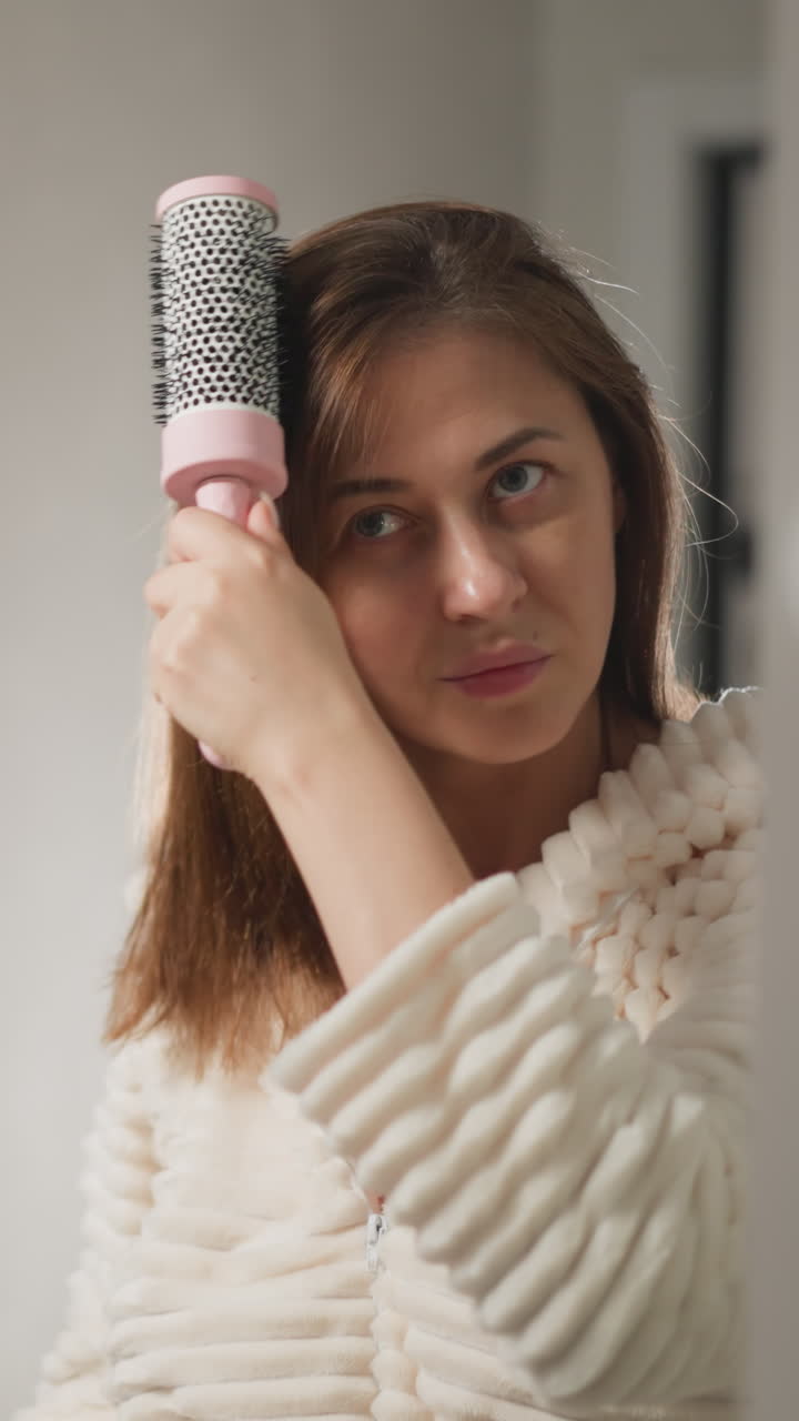 mujer combina el cabello con el cepillo después de tomar una ducha en el baño. mujer endereza el cabello mojado con un peine en el baño contemporáneo con lámparas en cámara lenta