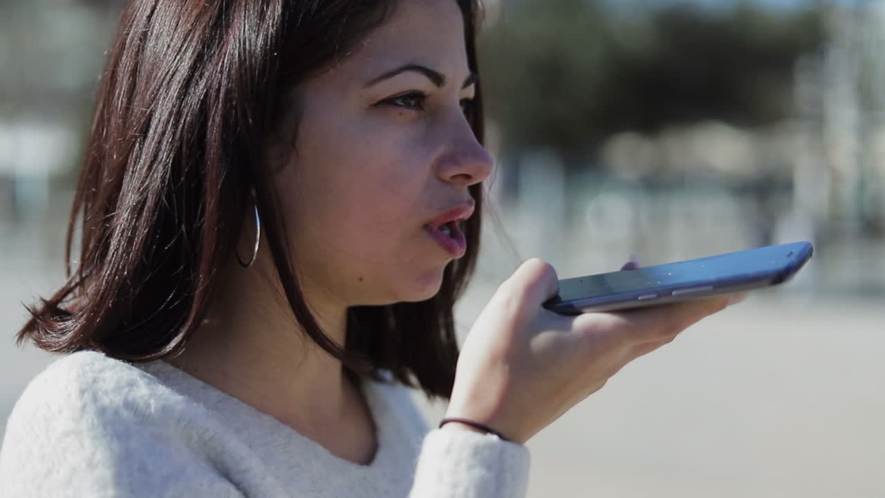 젊은 갈색 여성이 전화로 목소리 메시지를 기록하는 데 초점을 맞추고 있습니다.