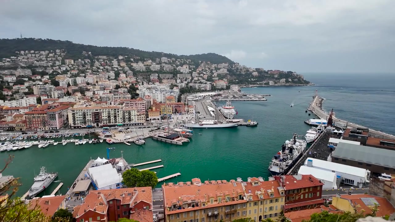 Vista dall'alto su Port Lympia a Nizza, che mostra barche, il porto turistico e un denso paesaggio urbano collinare lungo il Mediterraneo sulla Costa Azzurra.