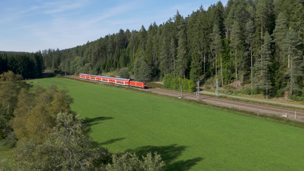 un tren rojo brillante de deutsche bahn acelerando a través de un paisaje verde exuberante, vista aérea