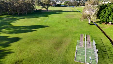 aerial footage of cricket practice nets in a lush park setting, captured in bright daylight with clear skies