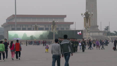 chinese troops march through tiananmen square with large electronic billboard background