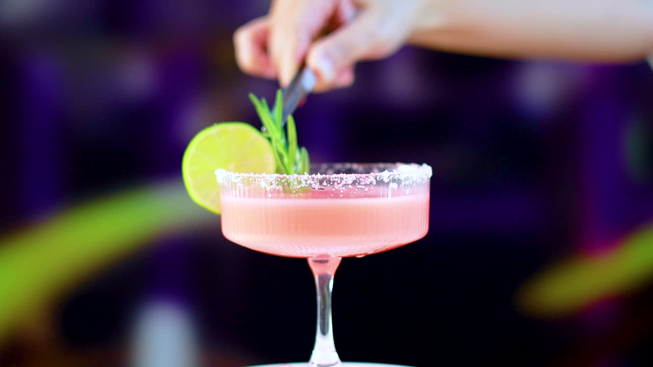 A vibrant margarita cocktail garnished with lime and rosemary, set against a colorful, blurred background with dynamic lighting