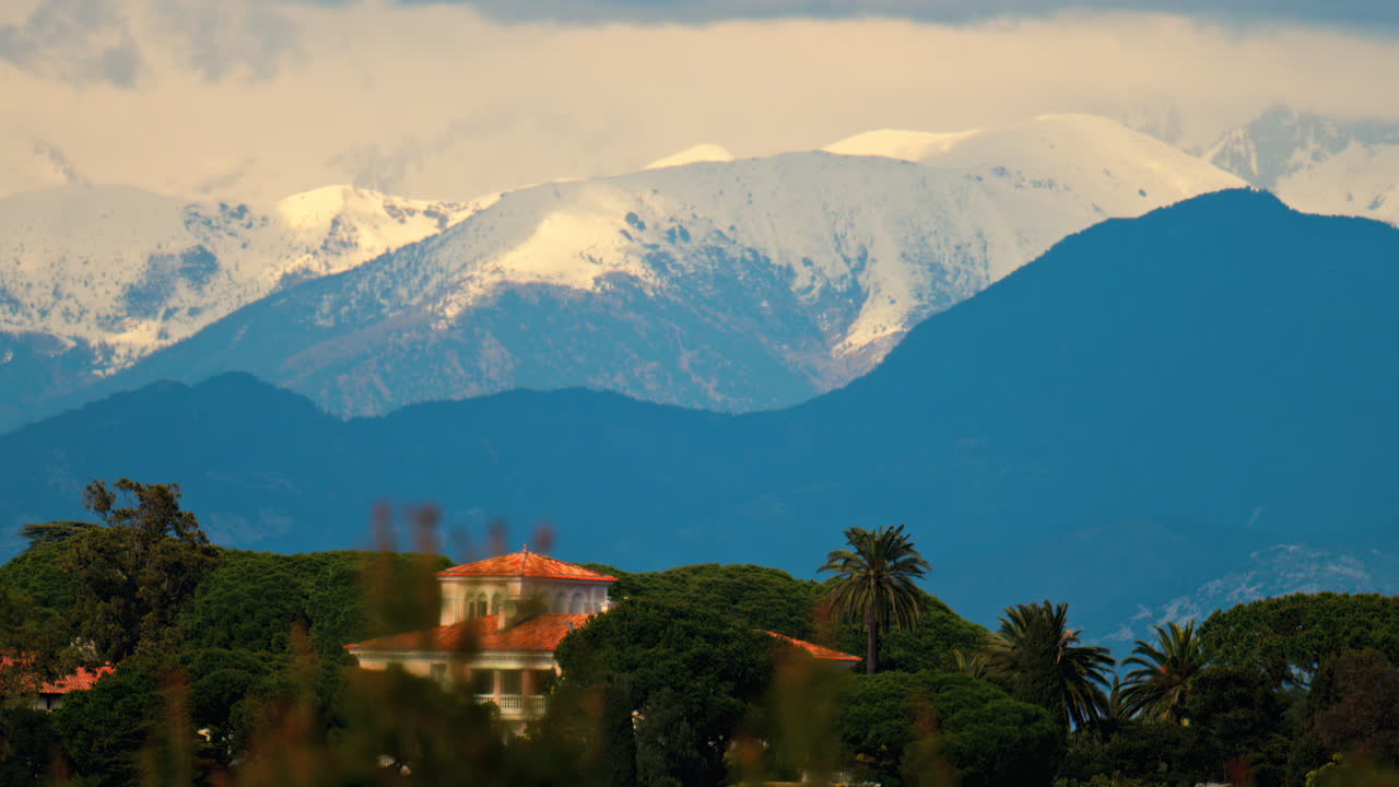 Distant view of orange villas surrounded by green trees with the mountains on the background on a cloudy day