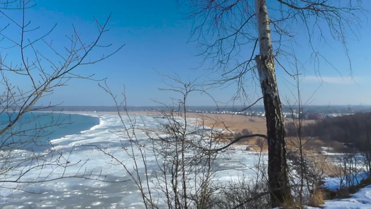 Gorgeous view from a high altitude winter white snow covered cliff bank of frozen Baltic sea with ice chunks and a grassy brown and reed filled beach shoreline during a sunny day in Tabasalu Estonia.