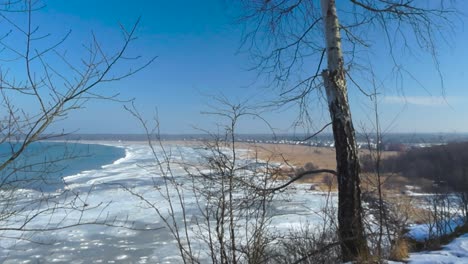 gorgeous view from a high altitude winter white snow covered cliff bank of frozen baltic sea with ice chunks and a grassy brown and reed filled beach shoreline during a sunny day in tabasalu estonia.