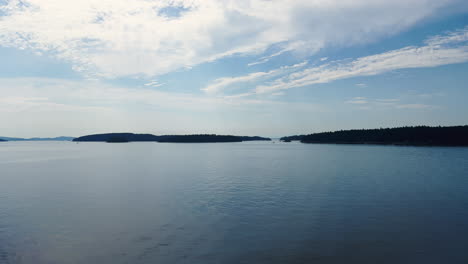 Wooded-Islands-in-the-ocean-shot-from-a-boat,-blue-sky,-handheld-gimbal