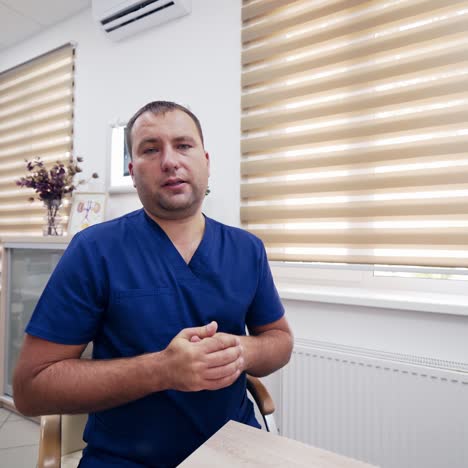 serious doctor doing distance video chat. specialist man in blue medical uniform giving a consultation to clients online in the office. telemedicine concept.
