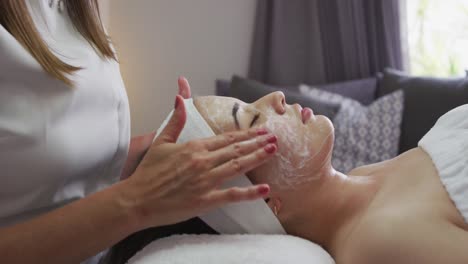 caucasian woman lying back while beautician gives her a facial