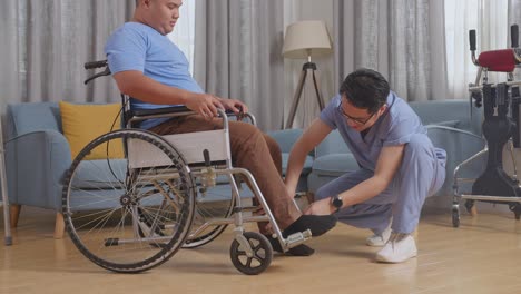 side view of asian male nurse helping a patient in wheelchair putting feet on footrest and pushing him to another room after a physical therapy at home