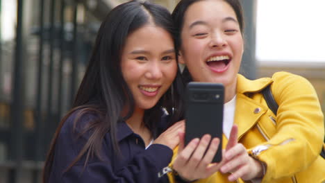 two smiling young female friends posing for selfie in urban setting together 2